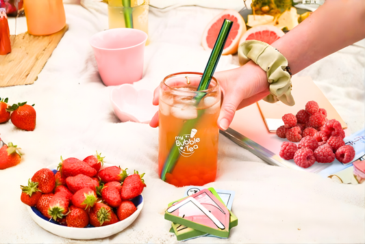 Een glas met bubble tea en ijs in op een dekentje met hierrond allemaal fruit en kopjes.