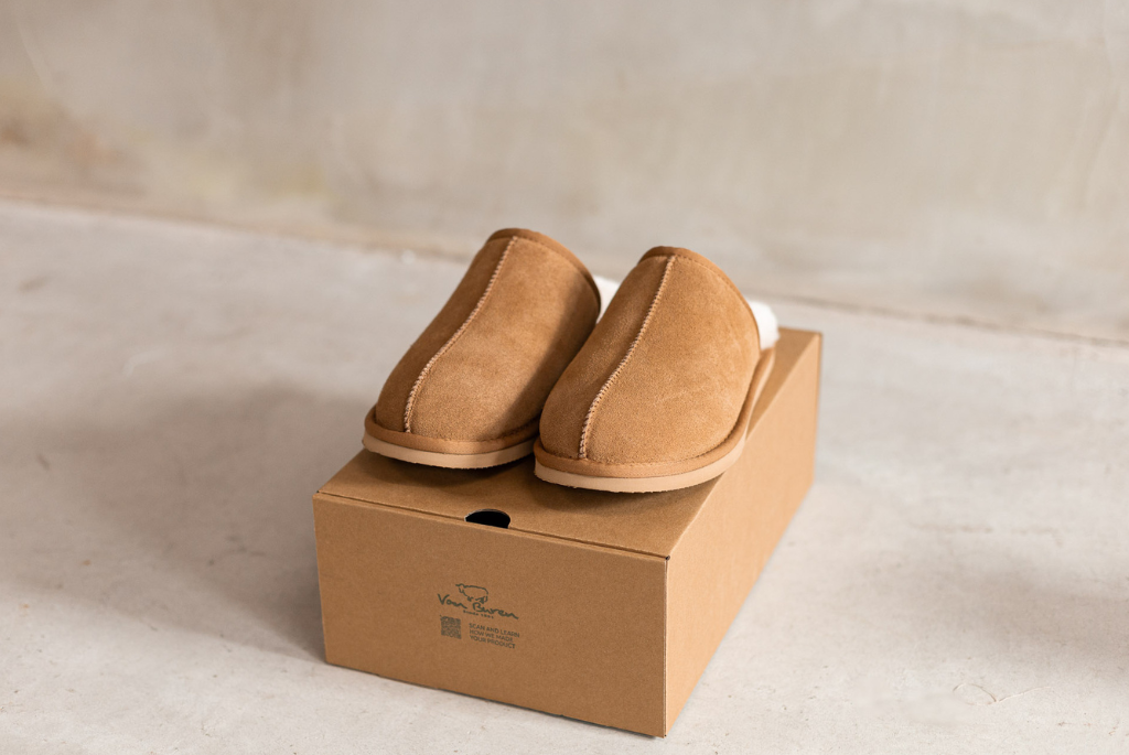 Een paar wollen sloffen in de kleur camel die op een doos staan in een betonnen kamer