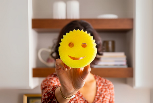 afbeelding waar een vrouw in haar keuken een scrub daddy smiley voor haar gezicht houd. Blog afbeelding over de meest gestelde vragen over scrub Daddy