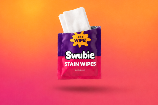 Swubie vlekken-doekje in zakformaat zwevend tegen een roze-oranje achtergrond, ideaal om vlekken onderweg snel te behandelen.
