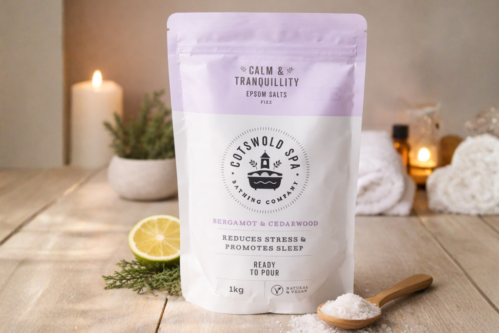 Een zak cotswold spa epsomzou calm tranquillity met een lepel zout voor en een kaars op de achtergrond