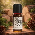 Een klein bruin glazen flesje met de tekst Natural Heroes essenstiële olie 209 cederhout. Op een boomstronk met afgekapte bomen achter van cederhout en dennennaalden.