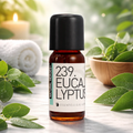 Een klein bruin glazen flesje met de tekst Natural Heroes essenstiële olie 239 eucalyptus in een spa setting met een handoek op de achtergrond en bladeren eucalyptus hier rond.