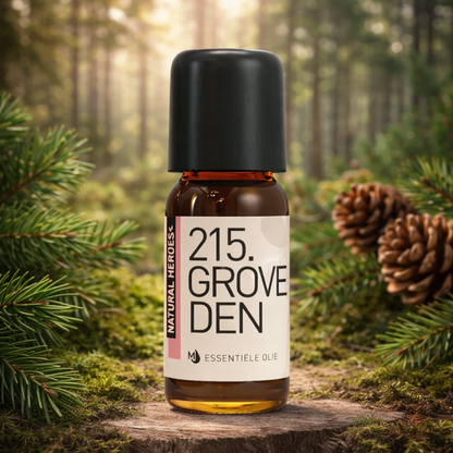 Een klein bruin glazen flesje met de tekst Natural Heroes essenstiële olie 215 groveden tussen de dennennaalden in een dennenbos op een afgekapte boomstronk.