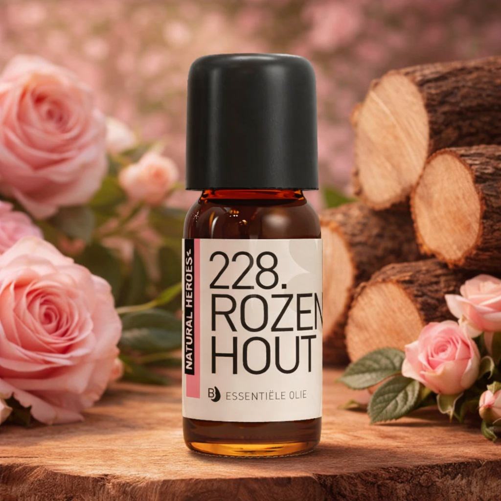 Een klein bruin glazen flesje met de tekst Natural Heroes essenstiële olie 228 rozenhout op een boomstronk met rozen en afgekapt hout hier rond.