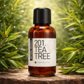 Een bruin glazen flesje met de tekst Natural Heroes essenstiële olie 201 Tea Tree op een stuk hout in een groene omgeving met veel theebladeren.