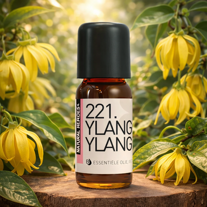 Een klein bruin glazen flesje met de tekst Natural Heroes essenstiële olie 221. ylangylang  tussen bloemen van Ylang Ylang en groen.